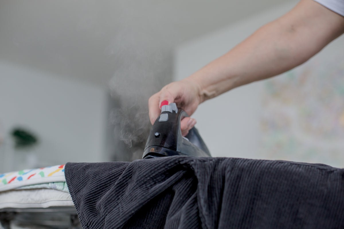Schwarzes Cordkleid wird gedämpft, zeigt die gerippte Textur des Cord-Overall-Kleiderstoffs