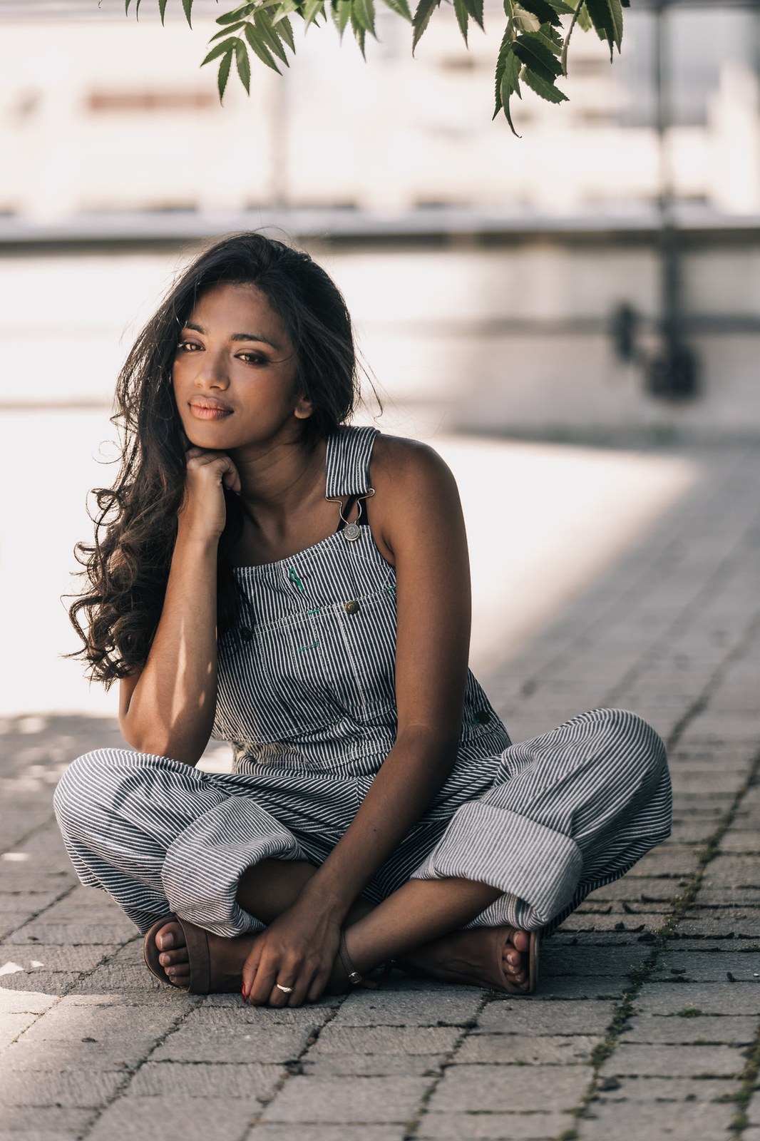 Woman in striped bib overalls sitting cross legged outdoors in a plus size overalls street style look